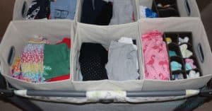 A clothes organizer for baby clothes created from a play yard with the bassinet feature in and 6 fabric storage bins sitting in the pack n play, with additional organizers for socks nested inside.