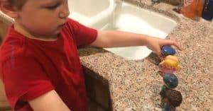 boy in red shirt lining up fisher price little people toys by a sink filled with water and soap