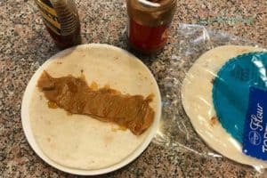 An easy kid friendly lunch idea- peanut butter and honey on a tortilla before rolling up, ingredients around the plate.