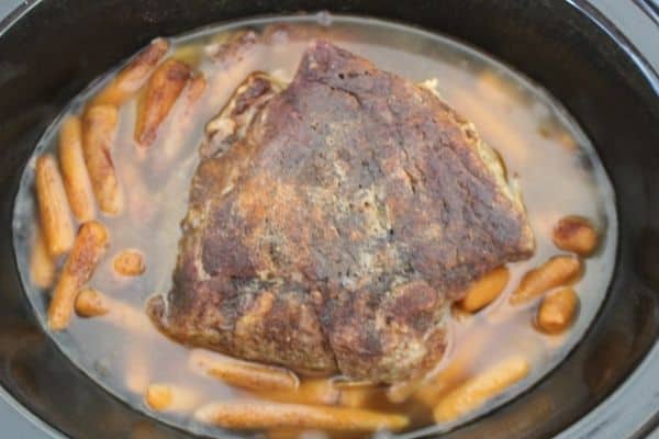 Pork shoulder after cooking but before shredding. Onions and carrots are submerged in liquid from the vegetables and roast.