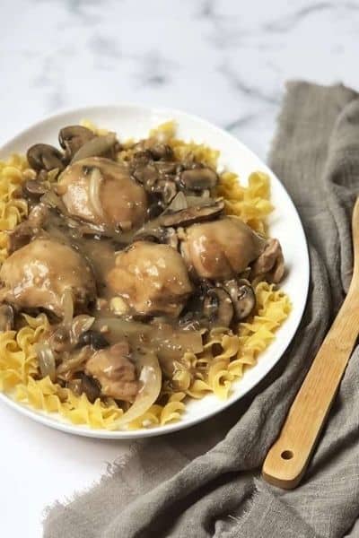 Crockpot Chicken Stroganoff over egg noodles on a white plate.