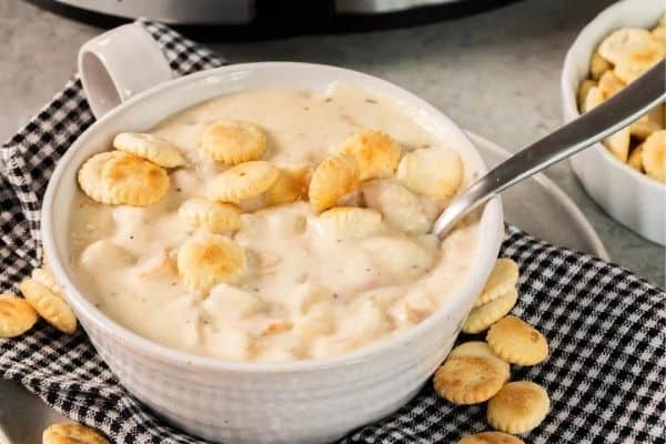 A large white cup filled with crockpot clam chowder and topped with oyster crackers.