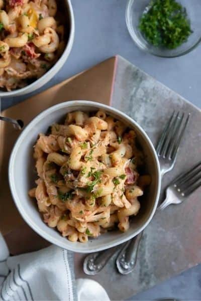 A bowl of crockpot creamy chicken pasta with forks, a second bowl, and decor in the background.