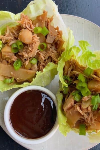 Two lettuce wraps on a white plate with a ramekin of sauce
