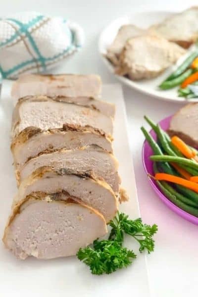 Pork loin sliced up in the left/center of the photo, with veggies and plates of it on the right side of the image