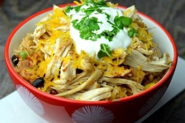 A red dish containing a taco bowl meal topped with sour cream, cheese, and cilantro.