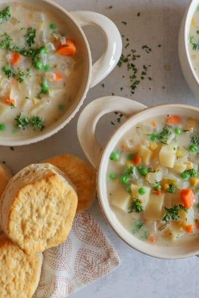 Overhead shot of white bowls filled with slow cooker veggie pot pie and biscuits to the side of the bowls.