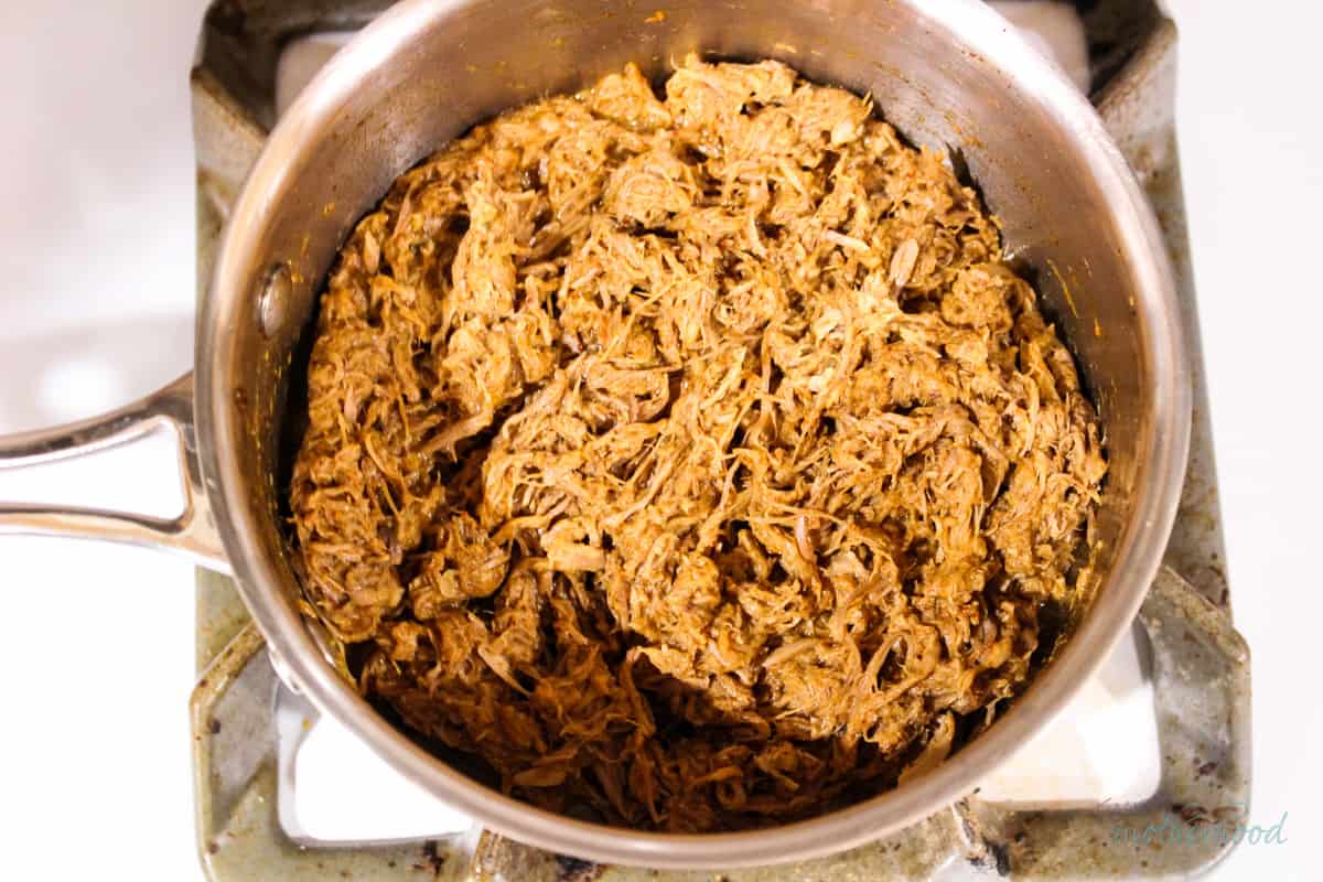 Leftover pulled pork and spices in saucepan after heating and further fork shredding