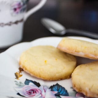 3 cookies on a white tea plate with purple and blue flower painting, a matching teacup in the background along with a spoon.