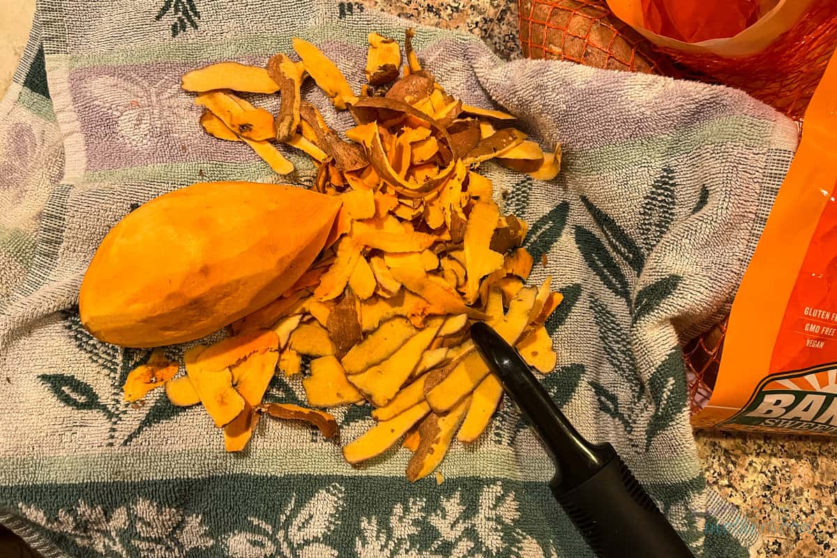 Peeled sweet potato with peeler sitting on kitchen towel