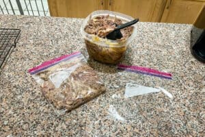 Container of leftover pulled pork on kitchen counter with ziplock bags and a measuring cup.