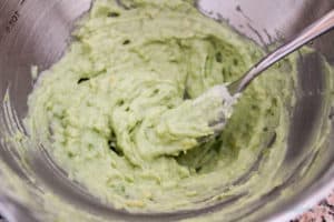 Avocado and greek yogurt in a stainless bowl after fork mixing.