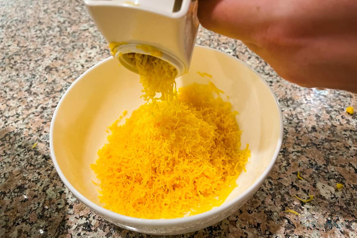 Shredding cheddar into a white bowl