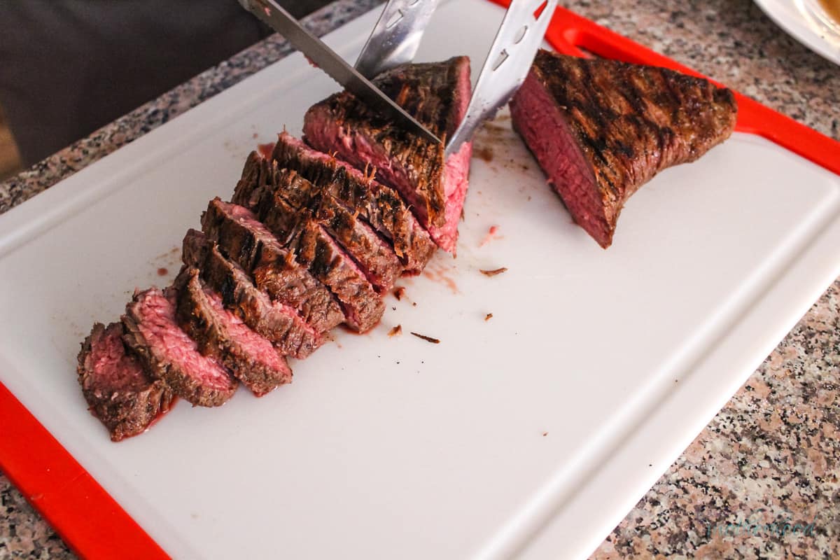 Slicing Tri Tip on cutting board with grill tongs and knife