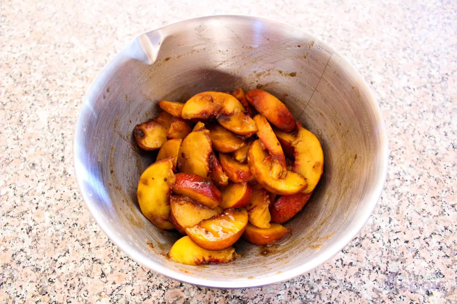 Prepared peaches with sugar and spices in mixing bowl.