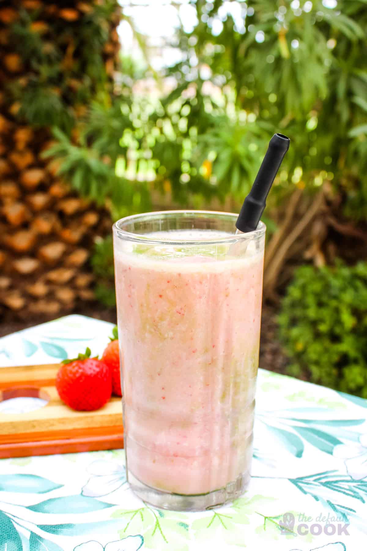 Smoothie on a table outdoors with strawberries and greenery behind it.