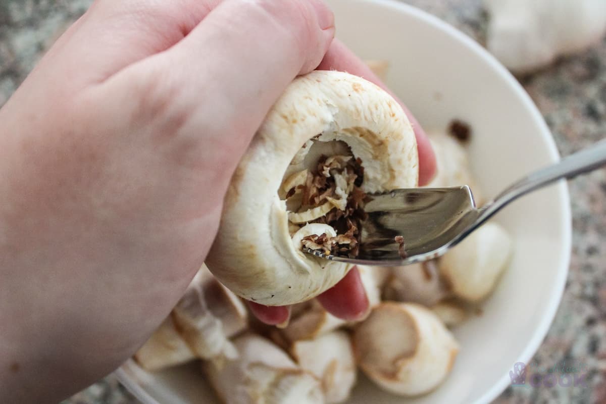 A mushroom cap being hollowed out with a grapefruit spoon.