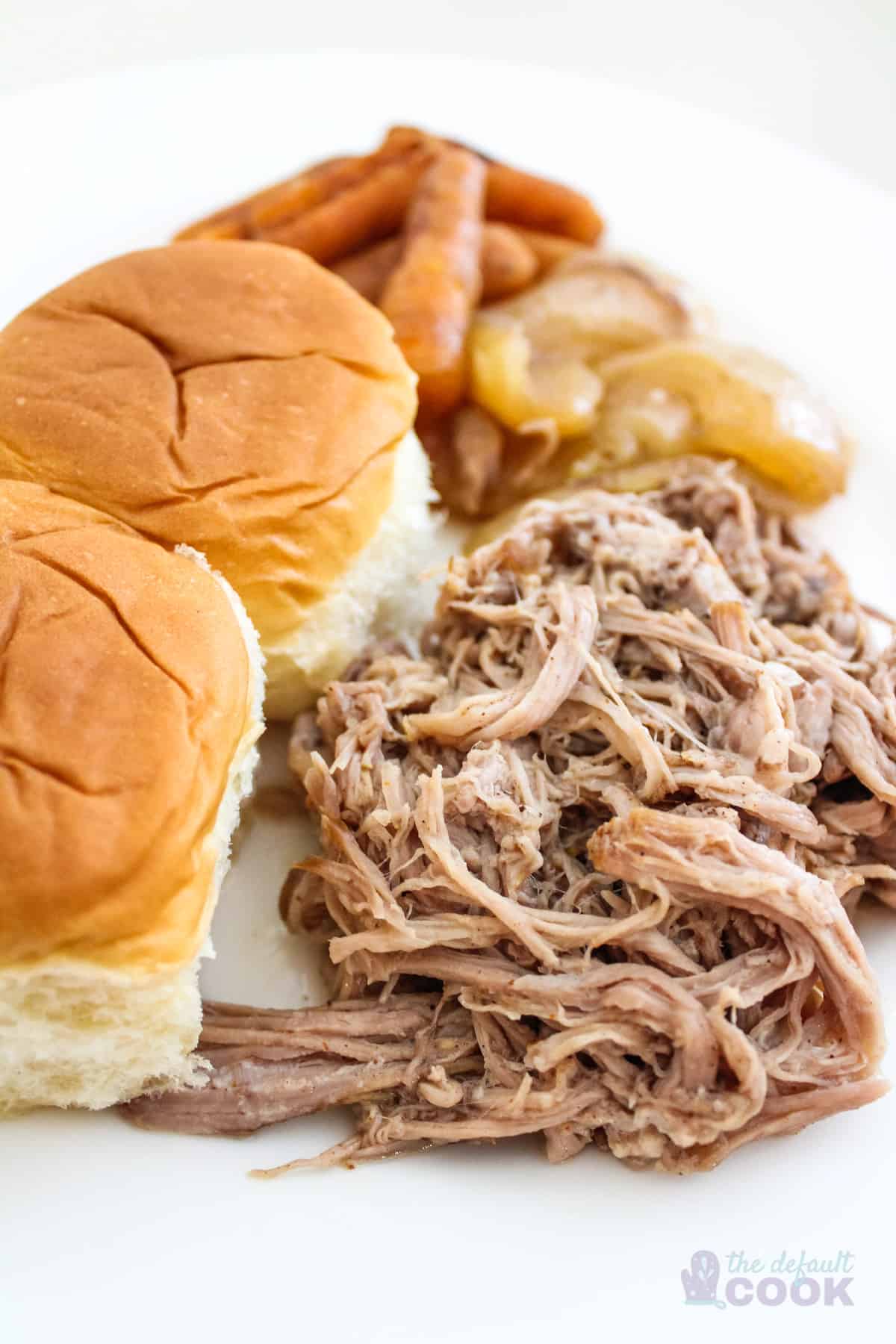 Pulled pork on white plate with onions, carrots, and hawaiian rolls.