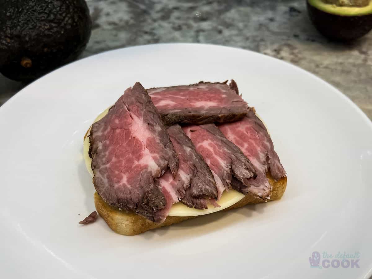 Slice of toasted bread with cheese and meat on top.