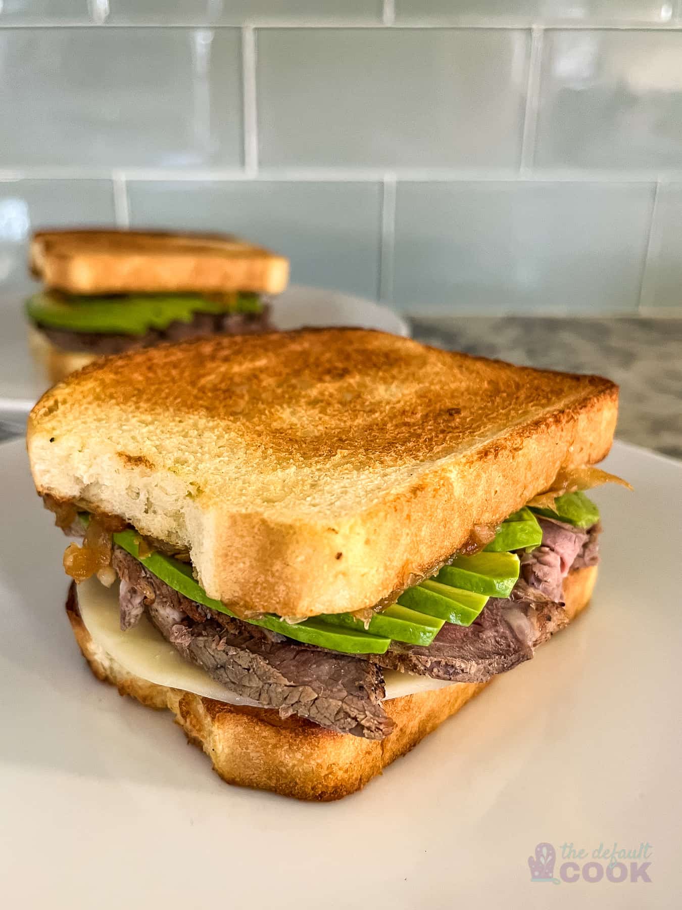 Two sandwiches on white plates with one in front of the other.