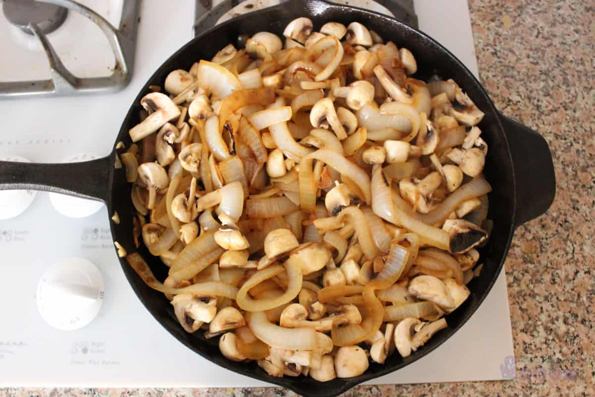 Onions cooked halfway with mushrooms just added in skillet.