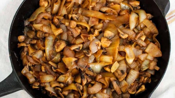 Skillet filled with caramelized mushrooms and onions on a kitchen towel.
