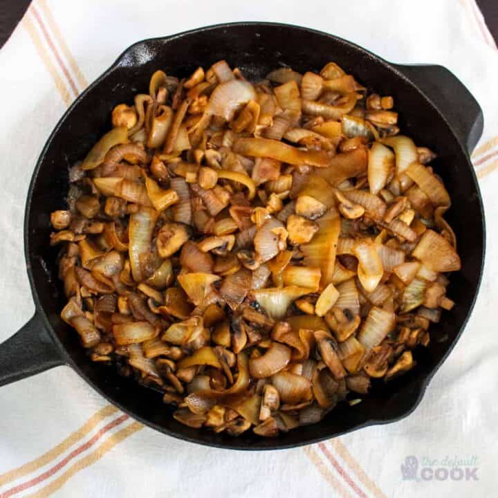 Skillet filled with caramelized mushrooms and onions on a kitchen towel.
