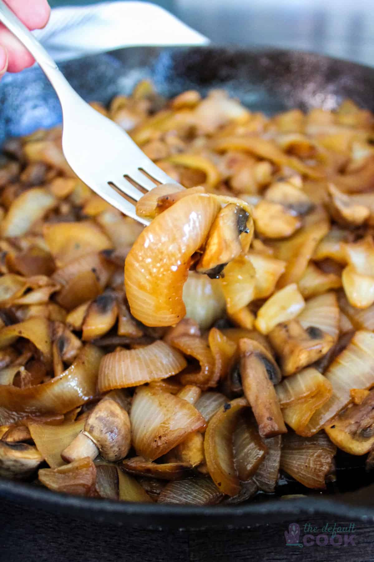 Caramelized onions and mushrooms in skillet with a fork holding a bite of them in front.