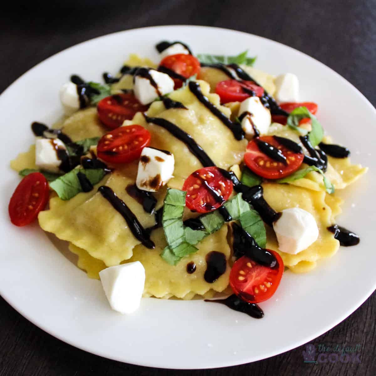 Ravioli on white plate topped with mozzarella pearls, cherry tomato halves, basil, and balsamic glaze.