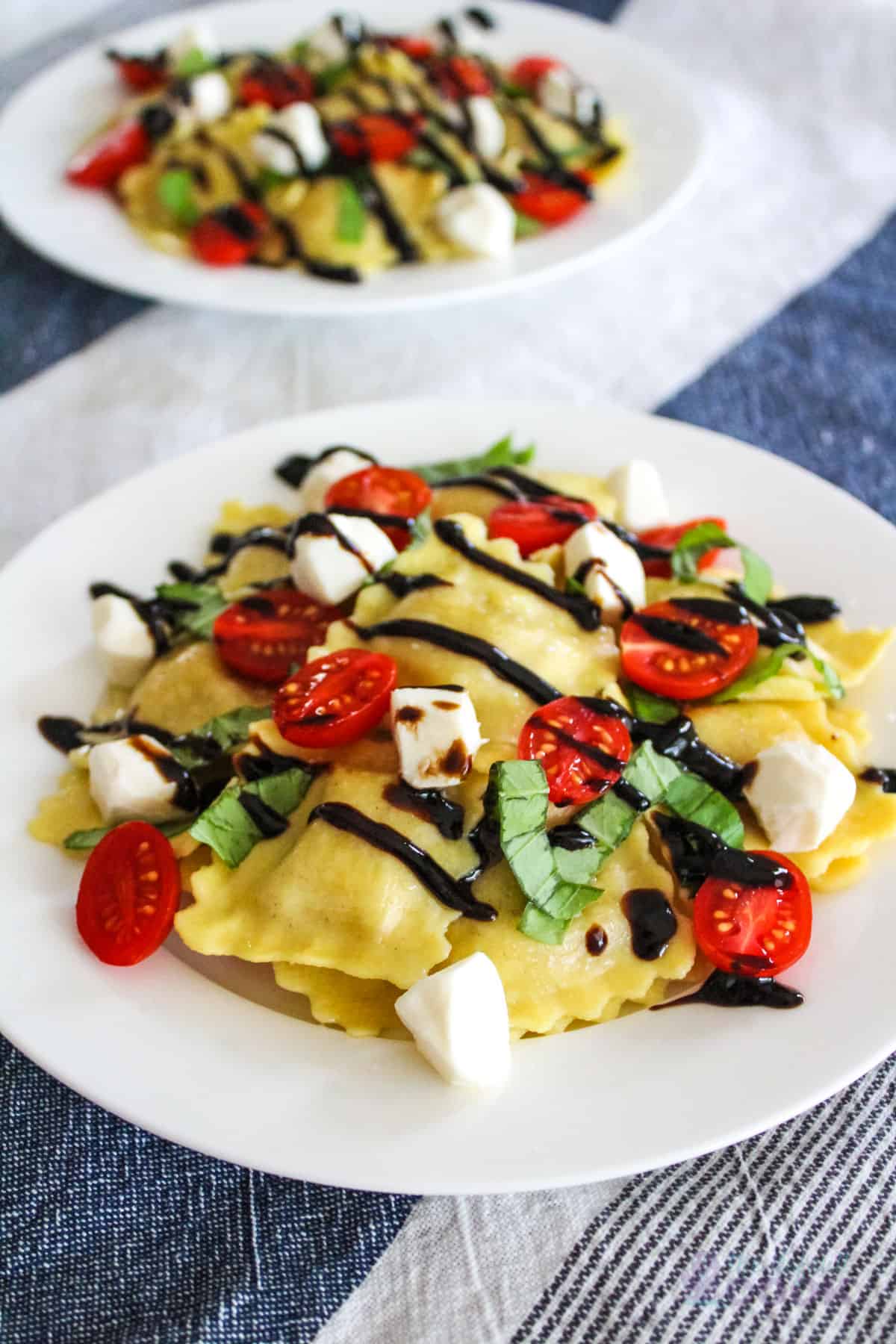 Two plates of caprese ravioli on a blue and white background.