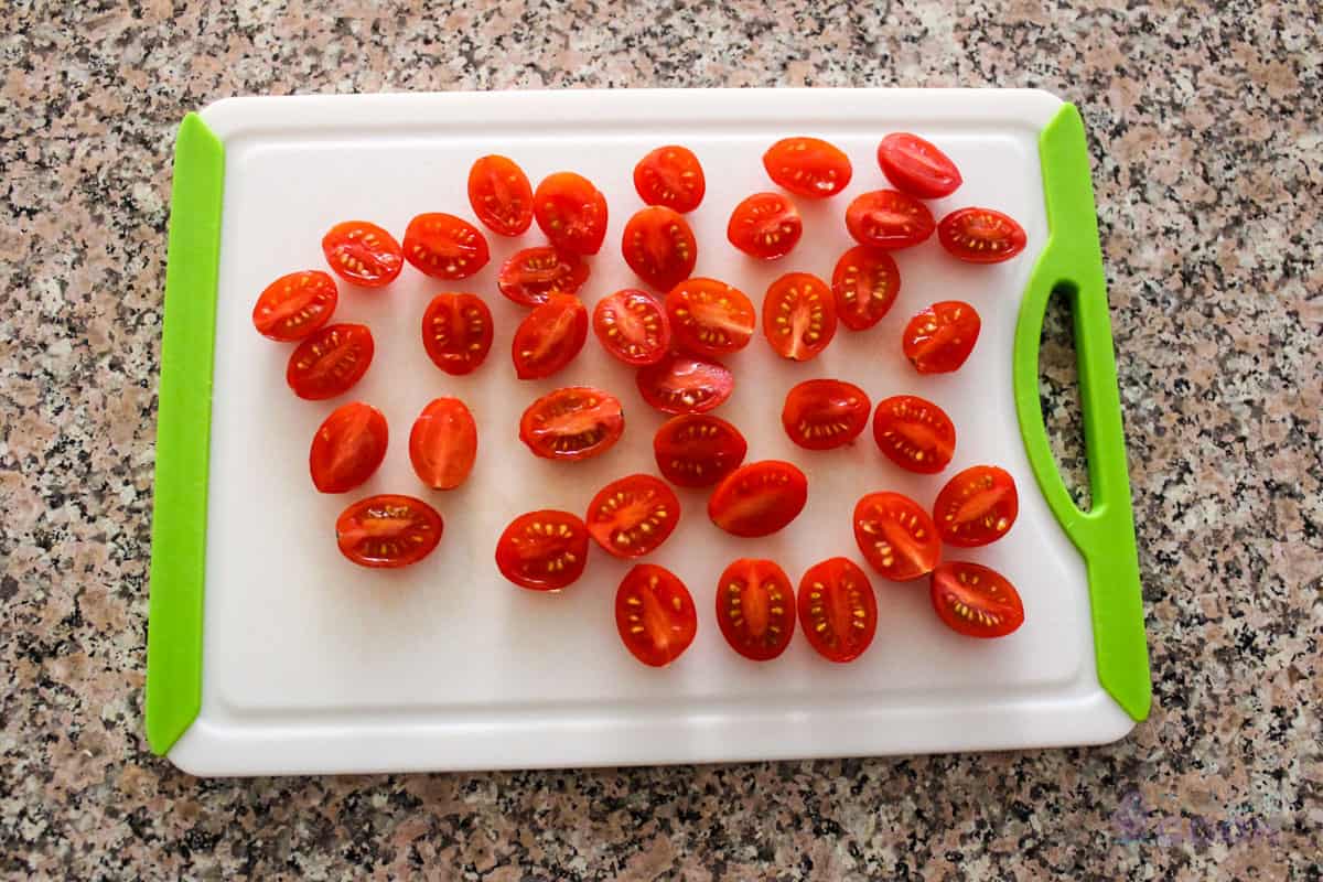 Cherry tomatoes cut in half on a cutting board.