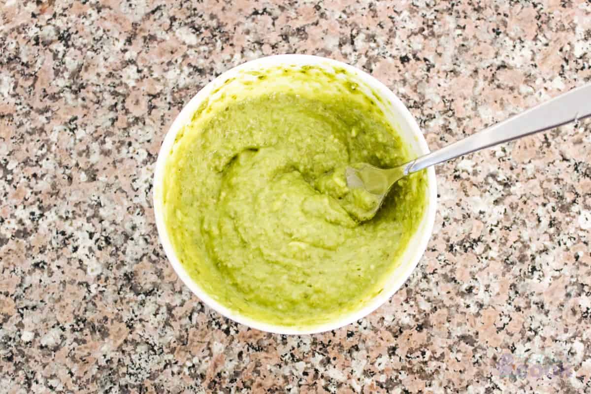 Pesto and butter mixed together with a fork in a small white bowl.