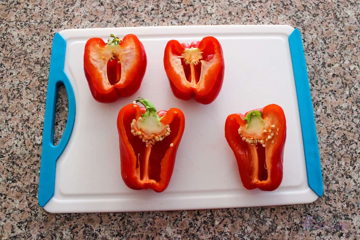 Rinsed red peppers sliced in half on cutting board.