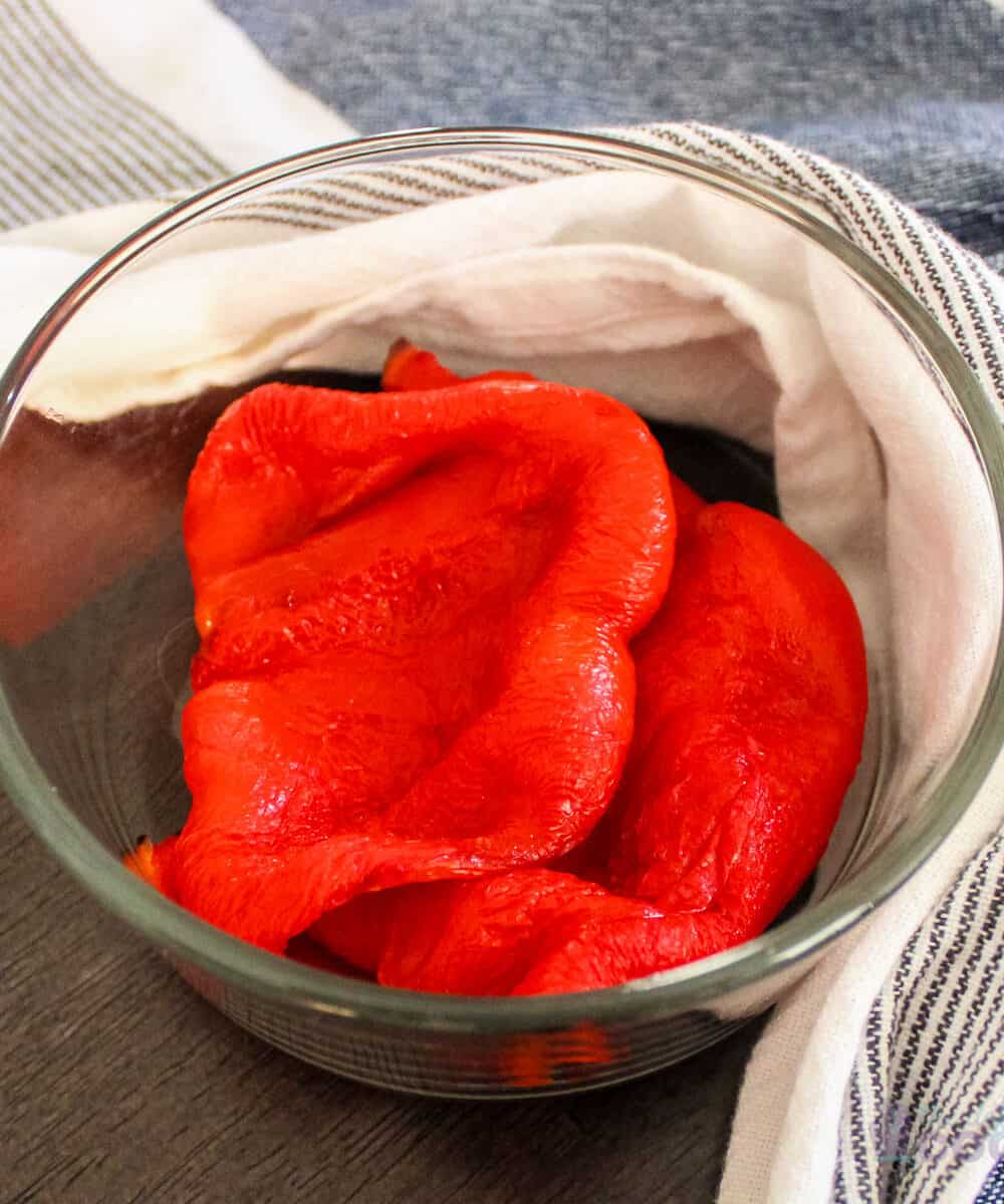 Roasted red peppers in a glass bowl with kitchen towel around it.