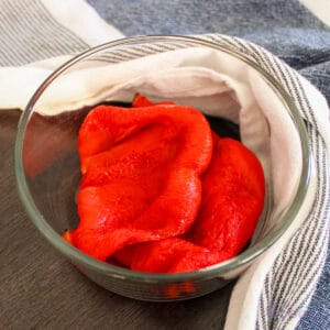 Roasted red peppers in a glass bowl with kitchen towel around it.