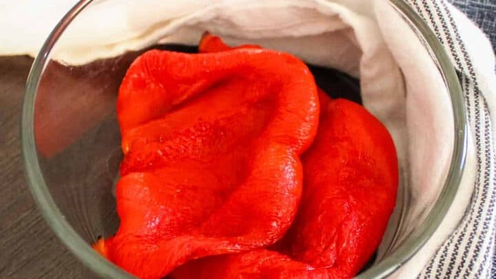 Roasted red peppers in a glass bowl with kitchen towel around it.