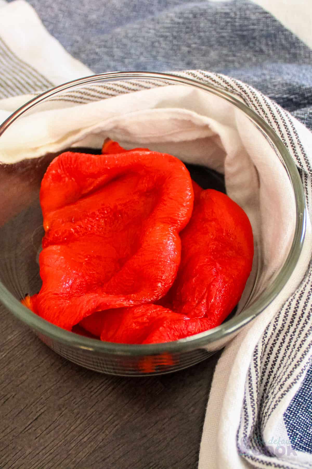Roasted red peppers in glass bowl with blue and white towl around it.