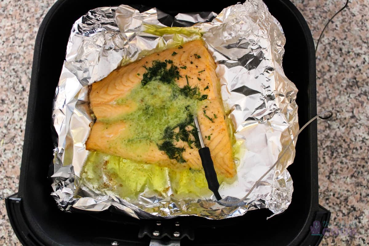 Finished salmon in air fryer basket lined with aluminum foil.