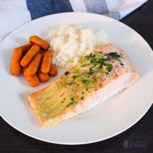 Pesto butter salmon on a white plate with rice and carrots.