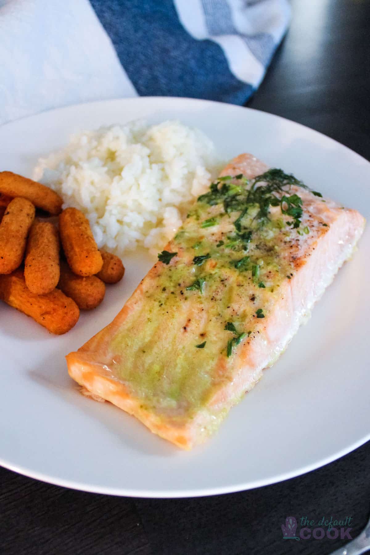 Pesto butter salmon on a white plate with rice and carrots.