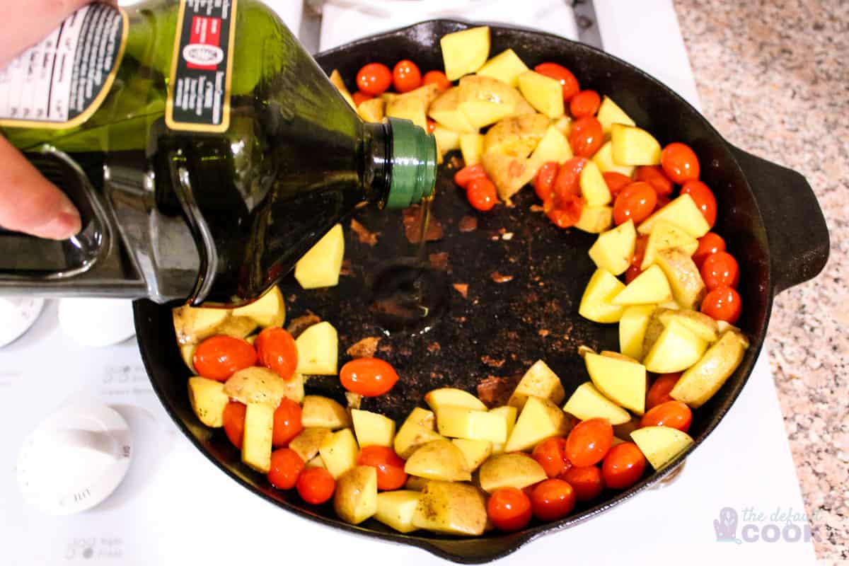 Ring of potatoes and tomatoes with open space in middle having olive oil drizzled in.