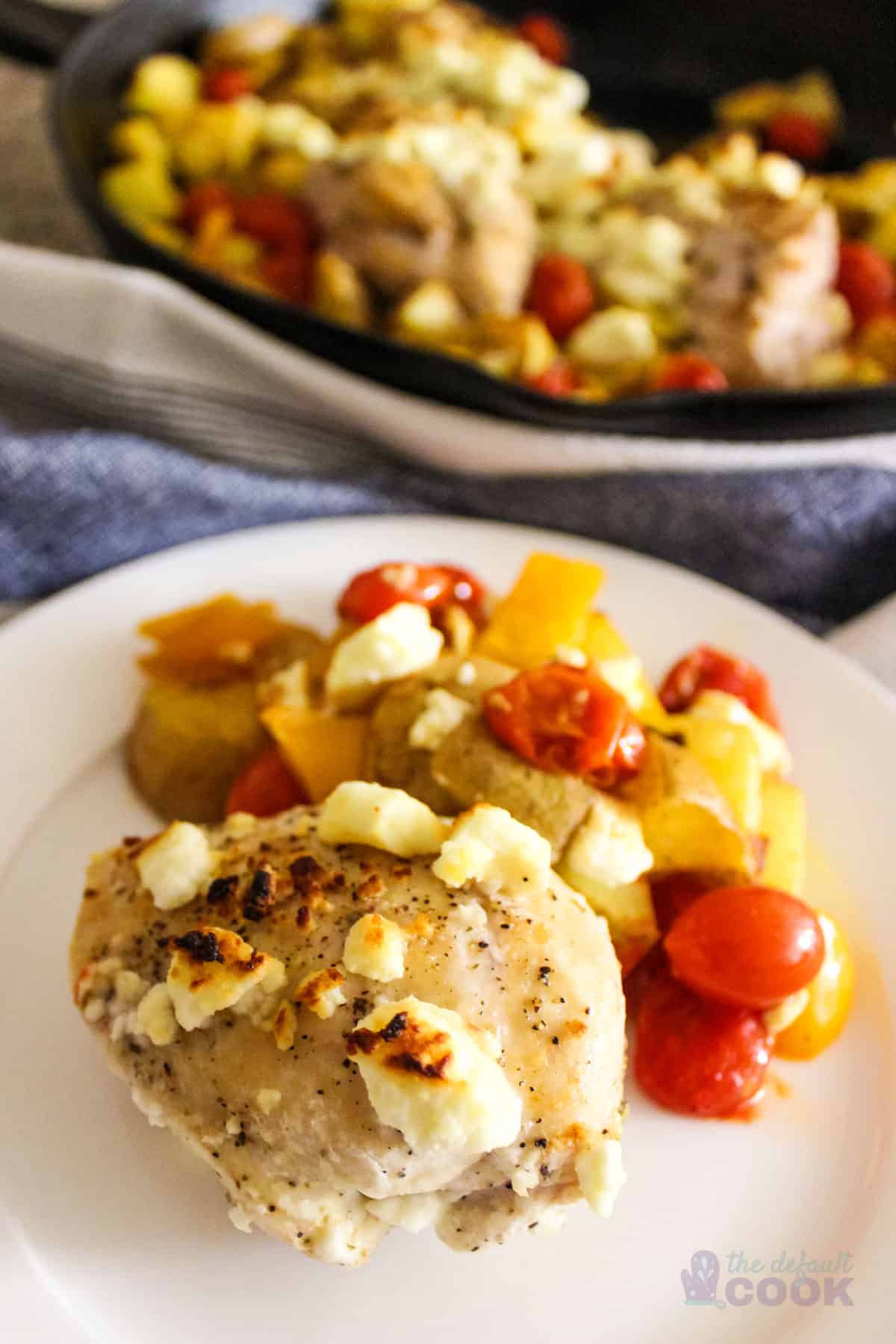 Plated baked feta chicken with serving skillet in the background.