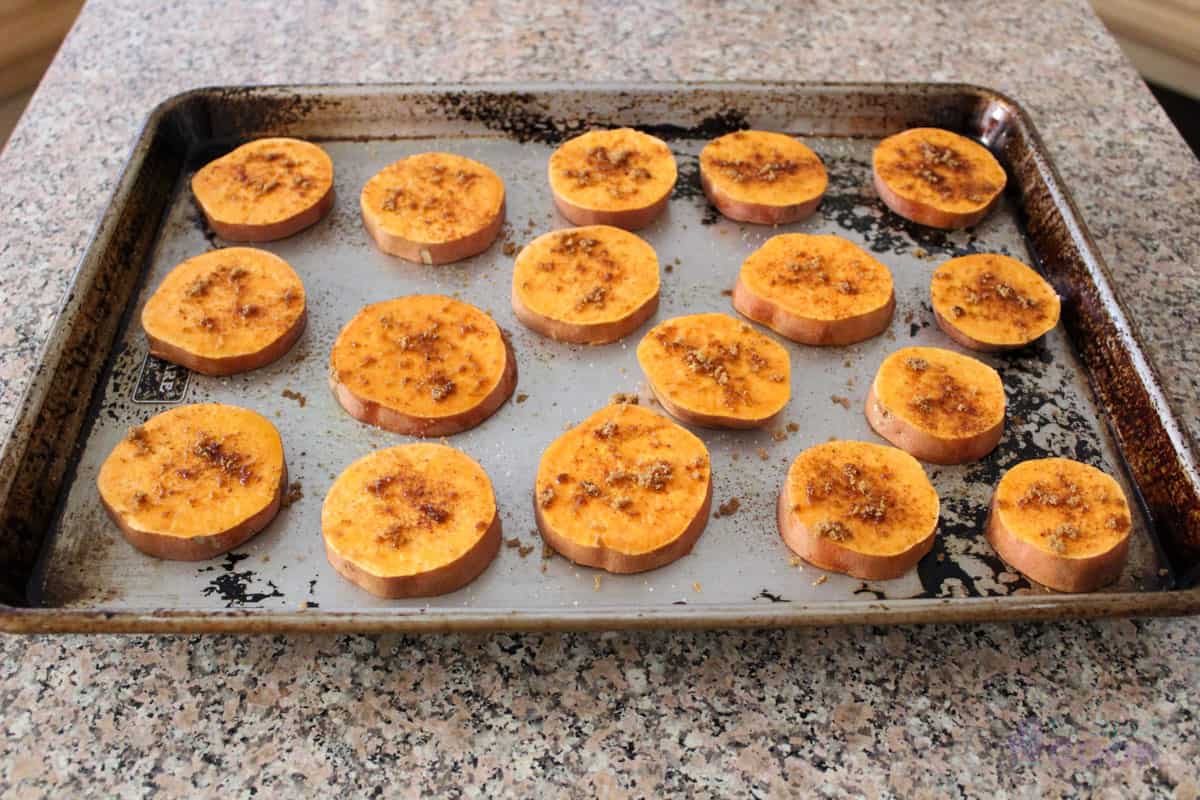 Sweet potato slices on a baking sheet and seasoned, ready for the oven.