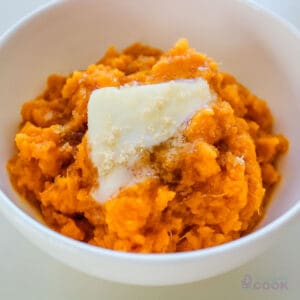 A white bowl filled with crock pot sweet potatoes and topped with butter that is melting.