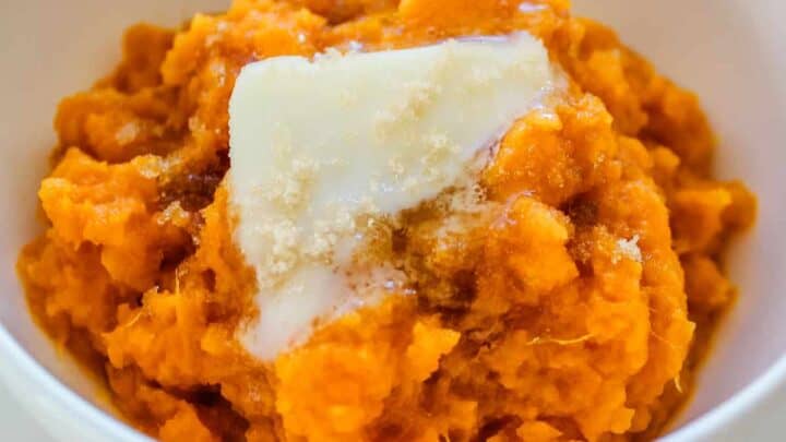A white bowl filled with crock pot sweet potatoes and topped with butter that is melting.
