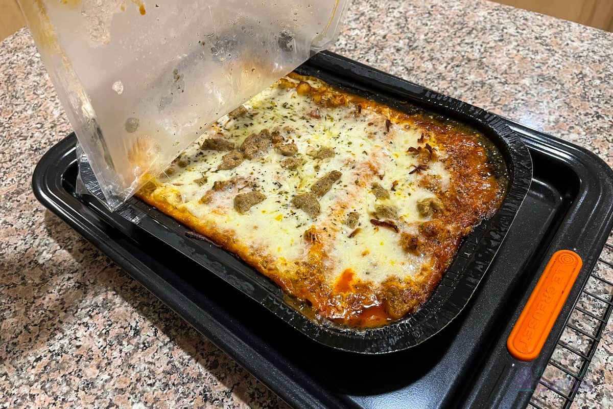 Peeling back the plastic film on the lasagna tray.