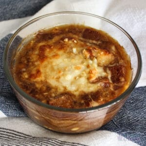 Bowl of French onion soup on blue and white towel.