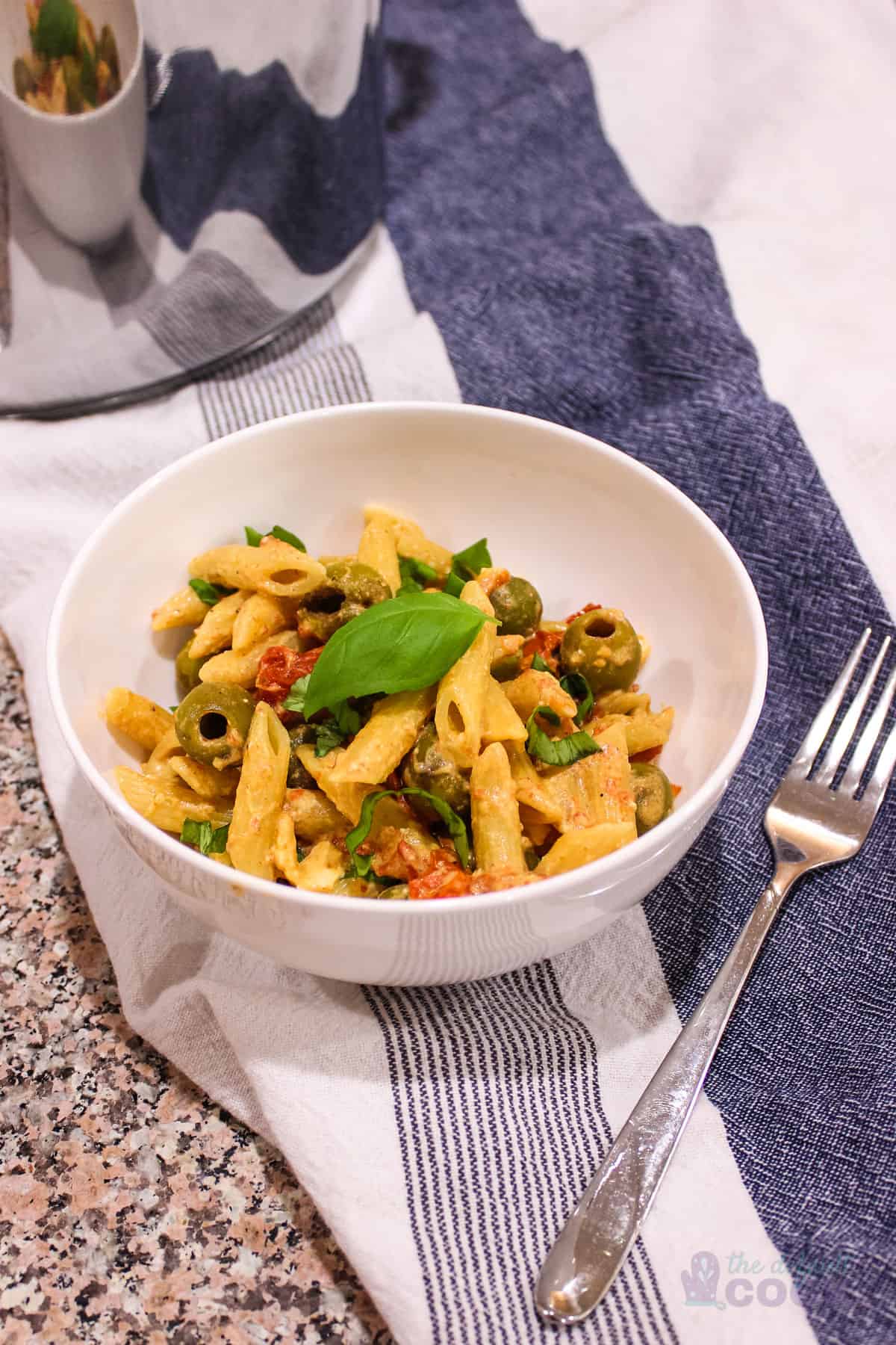 White bowl filled with baked feta pasta in front of pot with fork to the side.