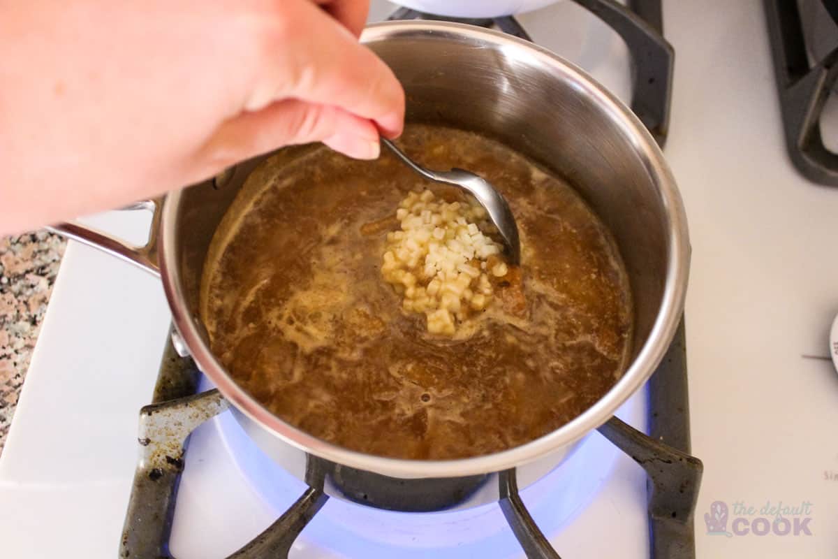 Mostly melted frozen soup in sauce pan, being gently stirred with a spoon.