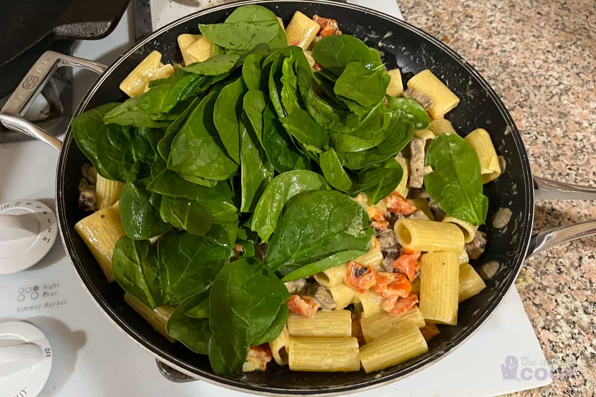 Skillet after adding pasta, with first handful of spinach on top.